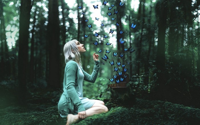 Woman in green dress releasing butterflies in a forest