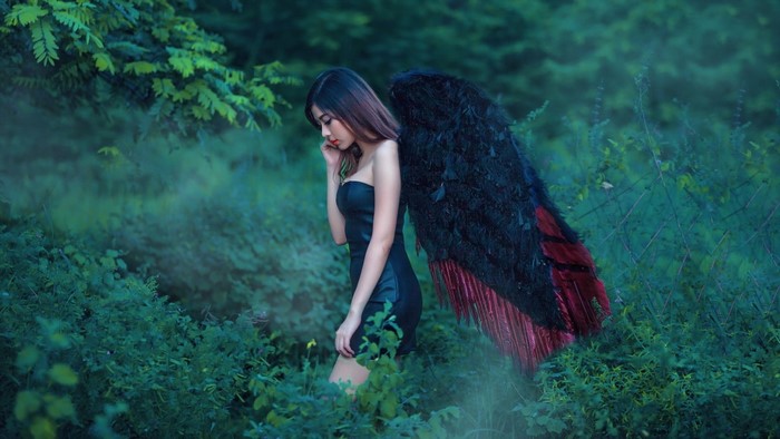 Woman with black wings in a green forest