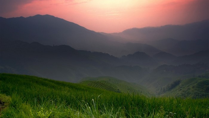 Misty mountains at sunrise with green fields