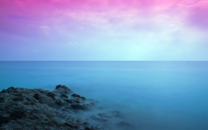 Ocean horizon with pink and blue sky and rocky shore