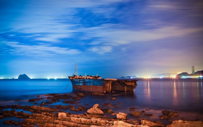 Shipwreck at night with distant cityscape and island