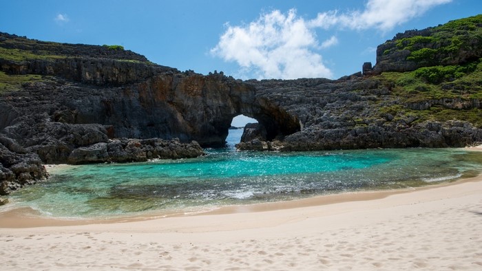 Arch rock formation over a turquoise lagoon and sandy beach