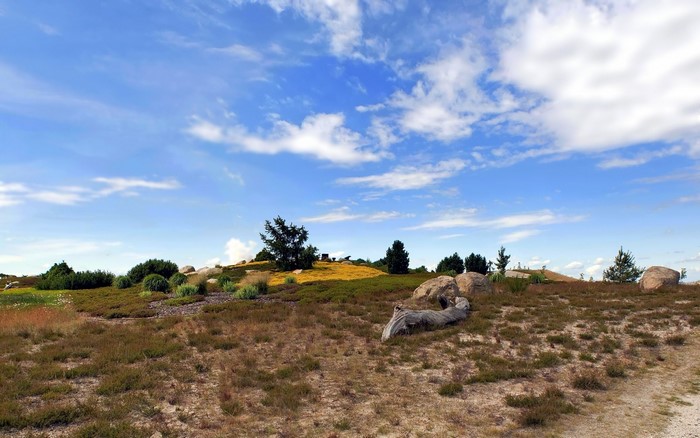 Rocky hill with sparse vegetation under a cloudy blue sky
