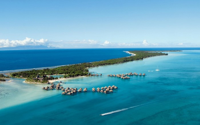 Overwater bungalows in a tropical lagoon with a distant island