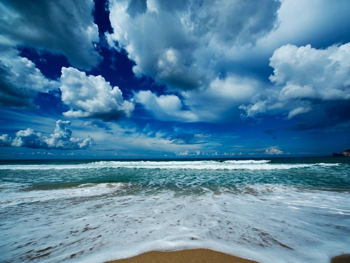 Ocean waves crashing on a sandy shore under a cloudy sky