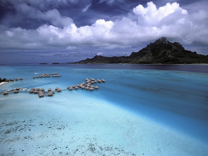 Overwater bungalows in a turquoise lagoon with a mountainous island