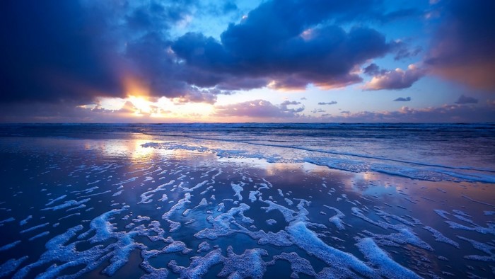 Sunset over the ocean with dramatic clouds and foamy waves