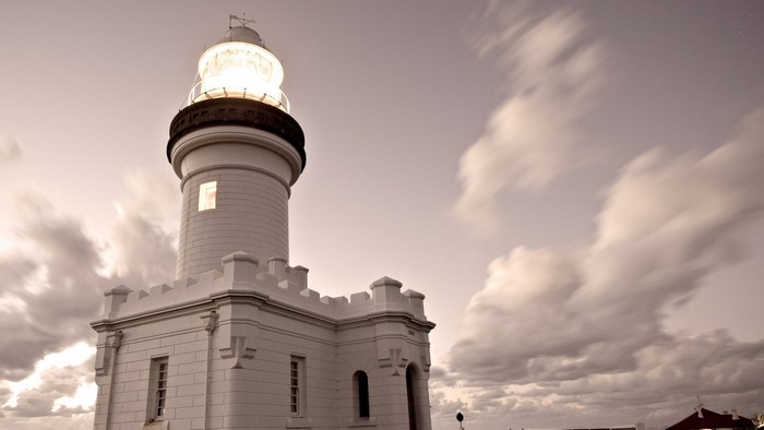 White lighthouse with a light on against a cloudy sky