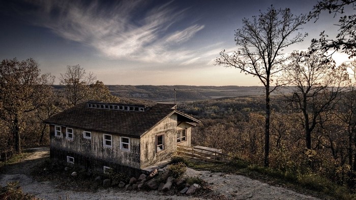 Rustic cabin on a hill overlooking a forest landscape at sunset