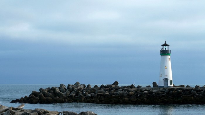 White lighthouse on a breakwater with ocean and cloudy sky