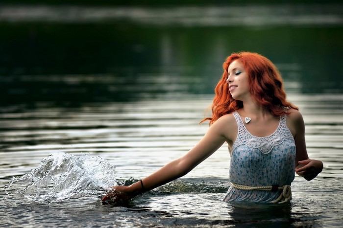 Woman with red hair splashing water in a lake