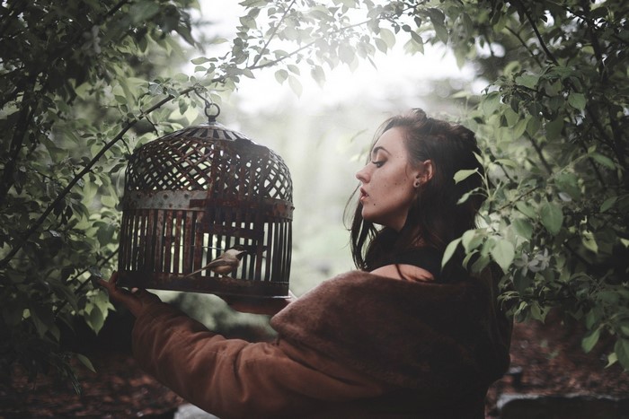 Woman holding a birdcage with a bird in a forest