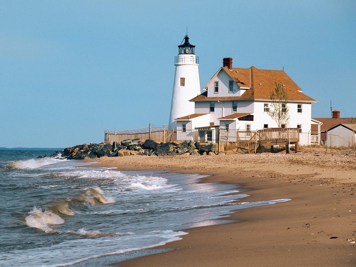 White lighthouse and keeper's house on a sandy beach with waves