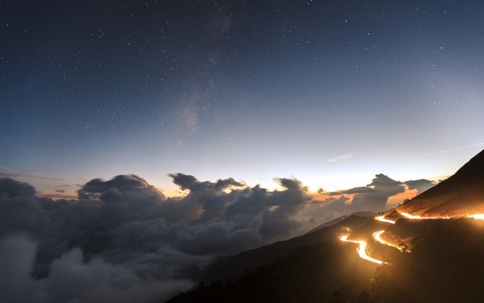 Mountain road at night with stars and clouds