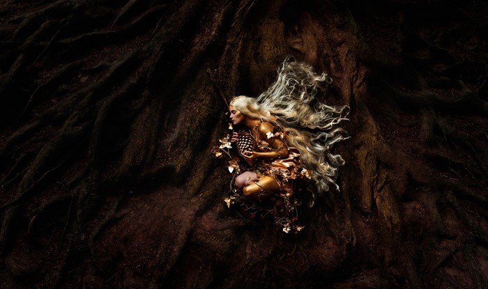 Golden woman with long blonde hair lying on tree roots