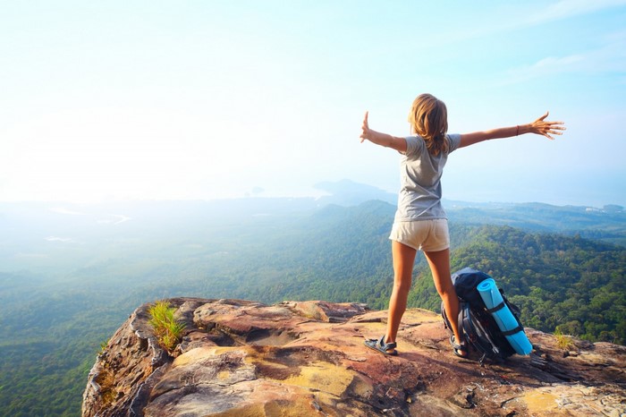 Woman with backpack on cliff overlooking mountains and sea