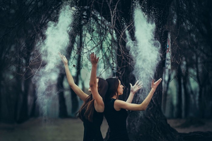 Two women in black dresses throwing dust in a forest