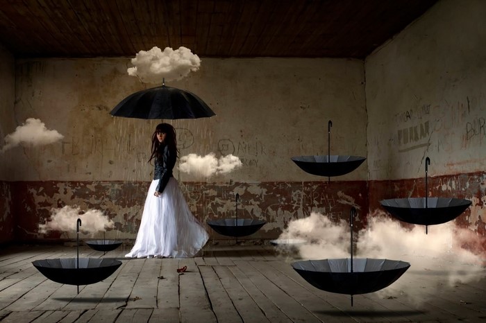 Woman in white dress under umbrella with floating clouds and umbrellas