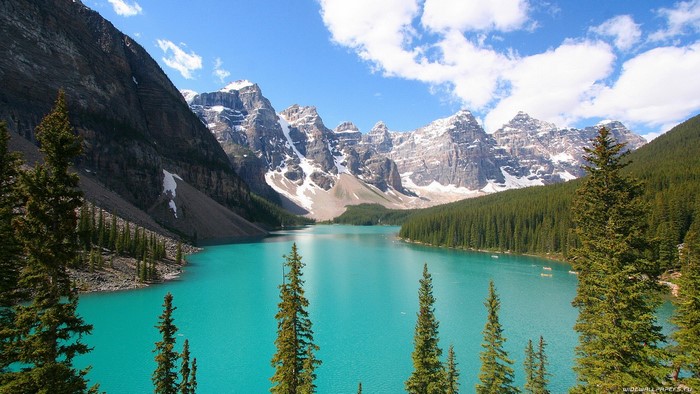Turquoise lake surrounded by pine trees and snow-capped mountains