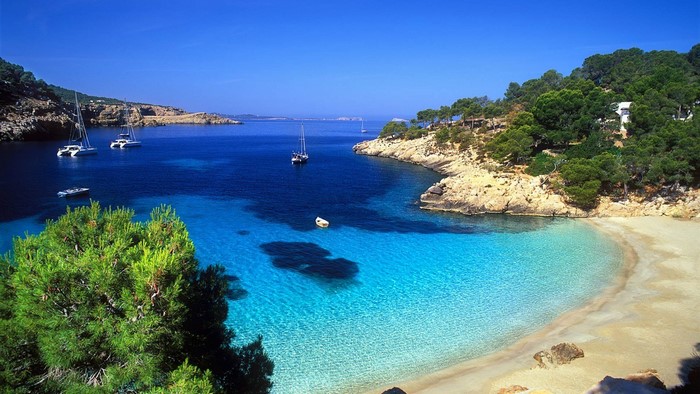 Boats in a tropical bay with a sandy beach and green hills