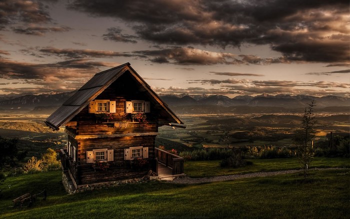 Wooden cabin on a hill overlooking mountains at sunset