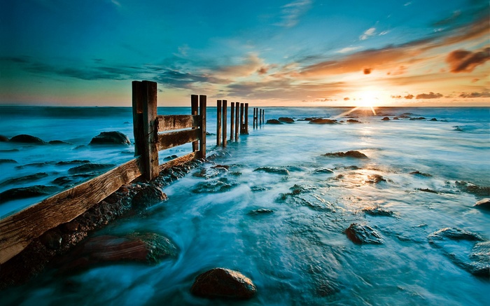 Wooden pier posts in the ocean at sunset