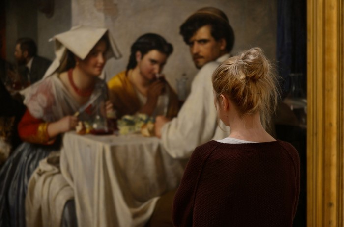 Woman looking at a painting of people at a table