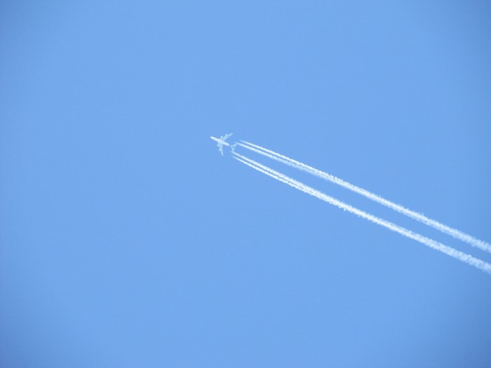 Airplane flying in a clear blue sky with contrails