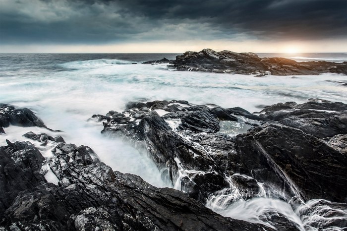 Waves crashing on rocky shore with stormy clouds
