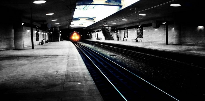 Train approaching a dark subway station with overhead lights