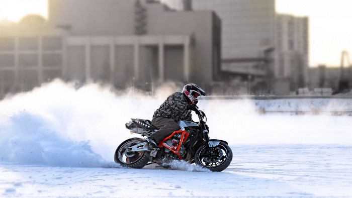 Motorcycle drifting in snow with buildings in background
