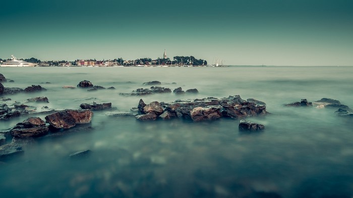 Rocky shore with a town and yachts in the distance