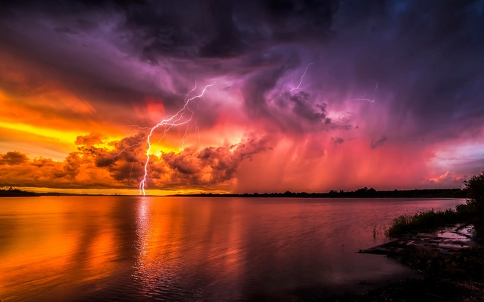 Lightning strikes over a lake during a colorful storm