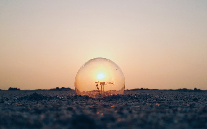 Light bulb with sun setting on sandy ground