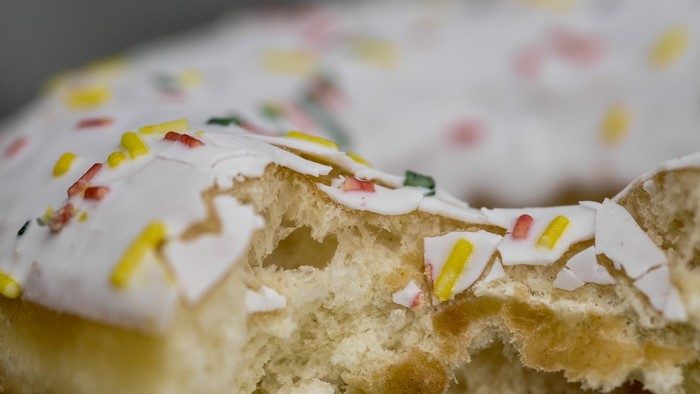 Close-up of a bitten donut with white icing and sprinkles
