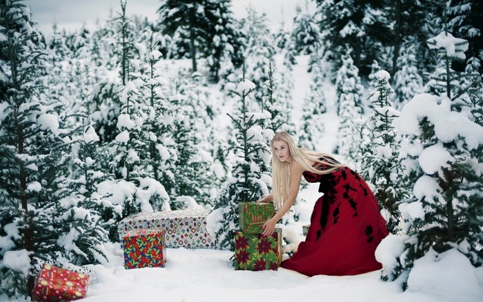 Woman in red dress with Christmas presents in snowy forest