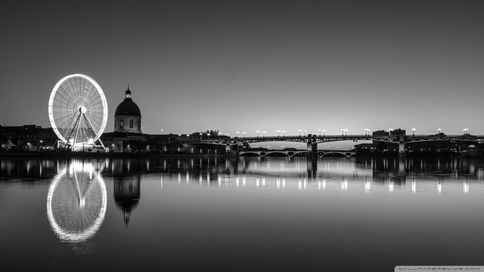 Black and white cityscape with Ferris wheel and bridges over river at dusk