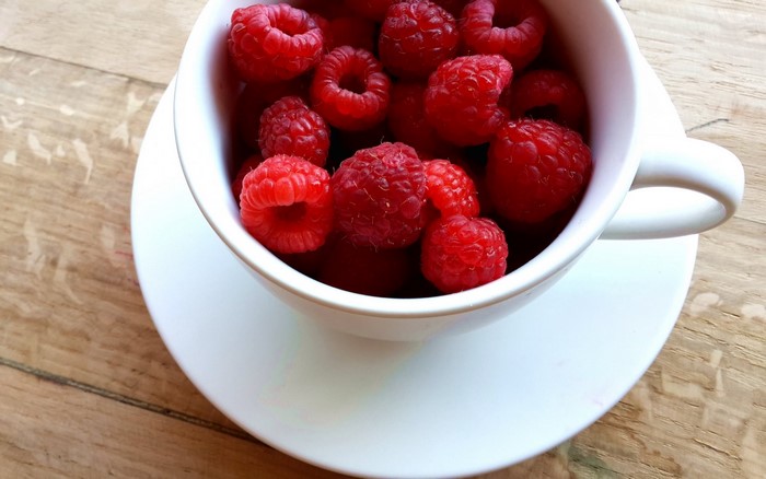 Raspberries in a white cup on a saucer