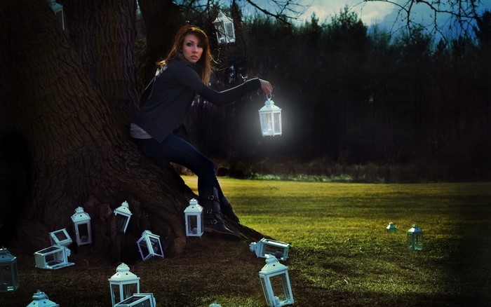 Woman sitting in a tree holding a lantern at night