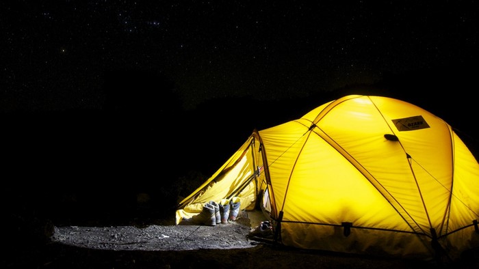 Yellow tent illuminated at night under starry sky
