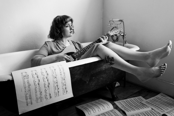 Woman playing guitar in a bathtub with sheet music