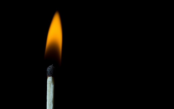A lit match with a bright orange flame against a black background