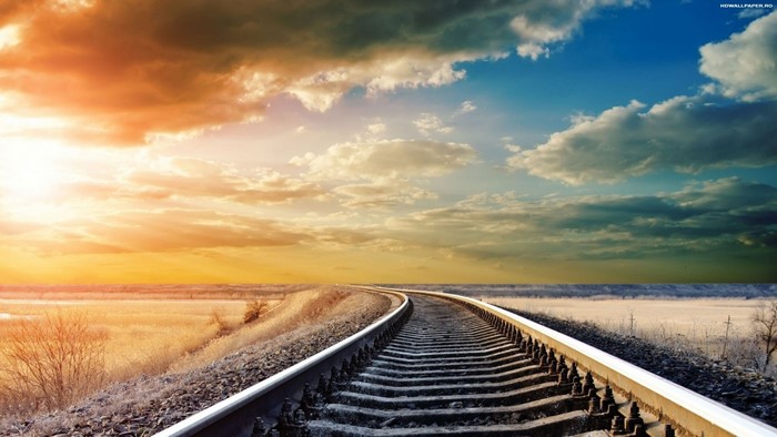 Railway tracks curving through a field at sunset