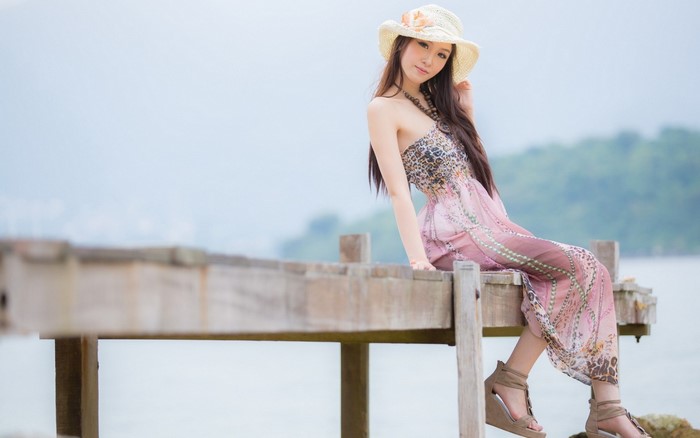 Asian woman in a pink dress and hat on a pier