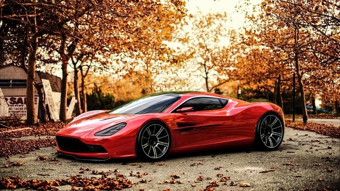 Red Aston Martin sports car on a leaf-covered road