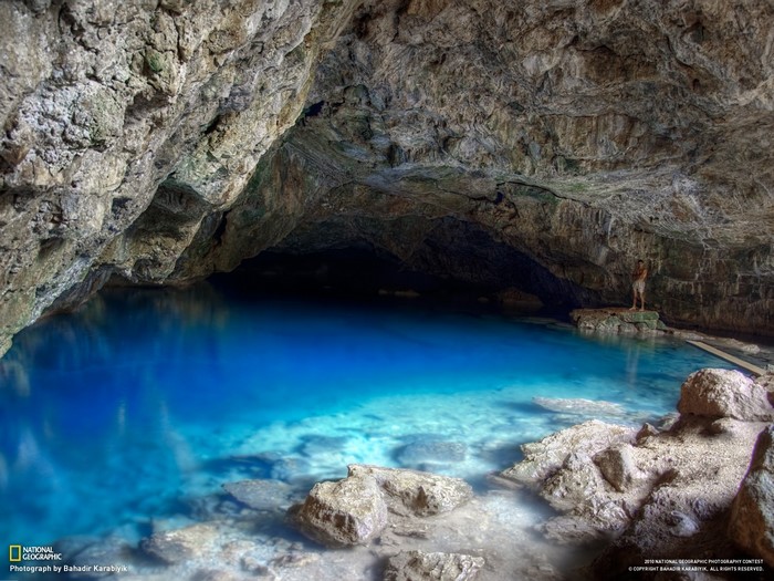 Man standing by a bright blue underground lake in a cave