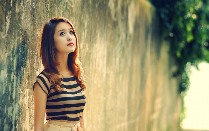 Young woman in striped shirt looking up against a textured wall