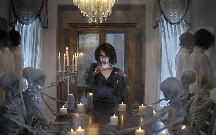 Woman with skeletons at a candlelit table