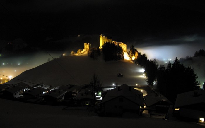 Castle on a snowy hill at night with village lights