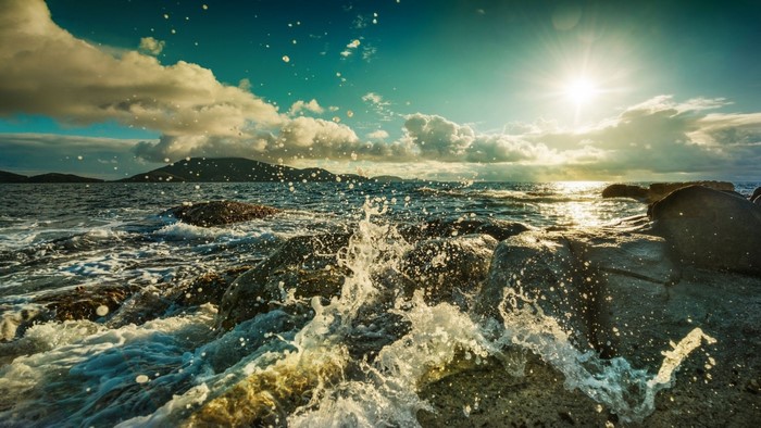 Waves crashing on rocks at sunset with sun flares